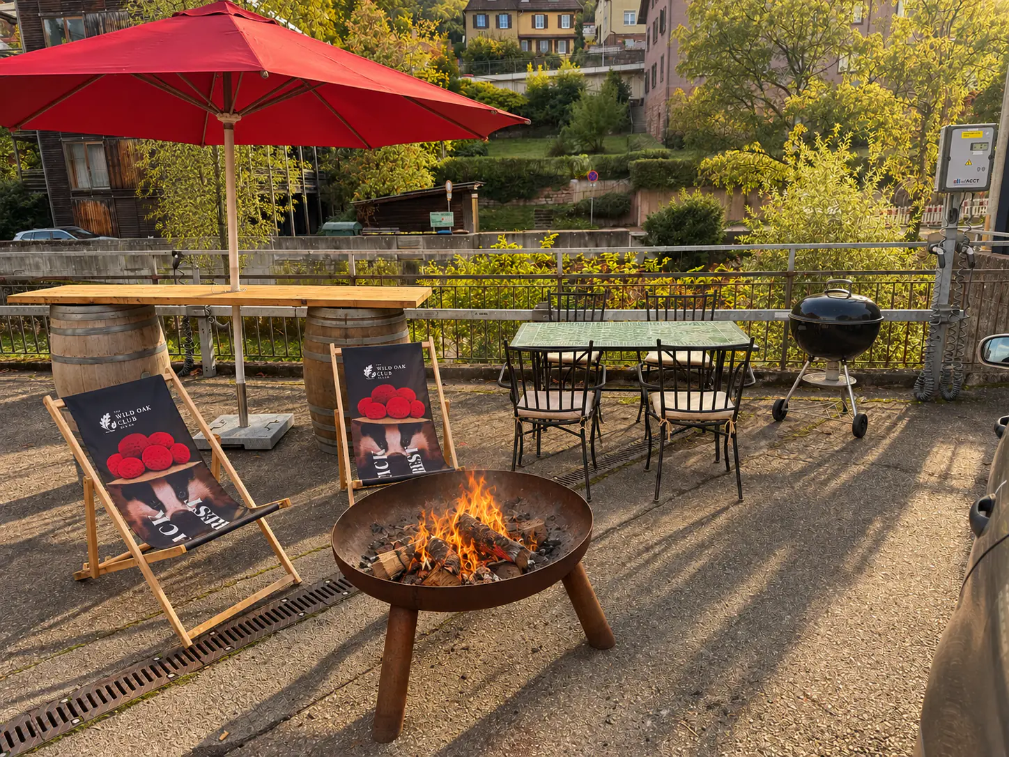 Outdoor area with a burning fire pit, deck chairs, grill and red parasols