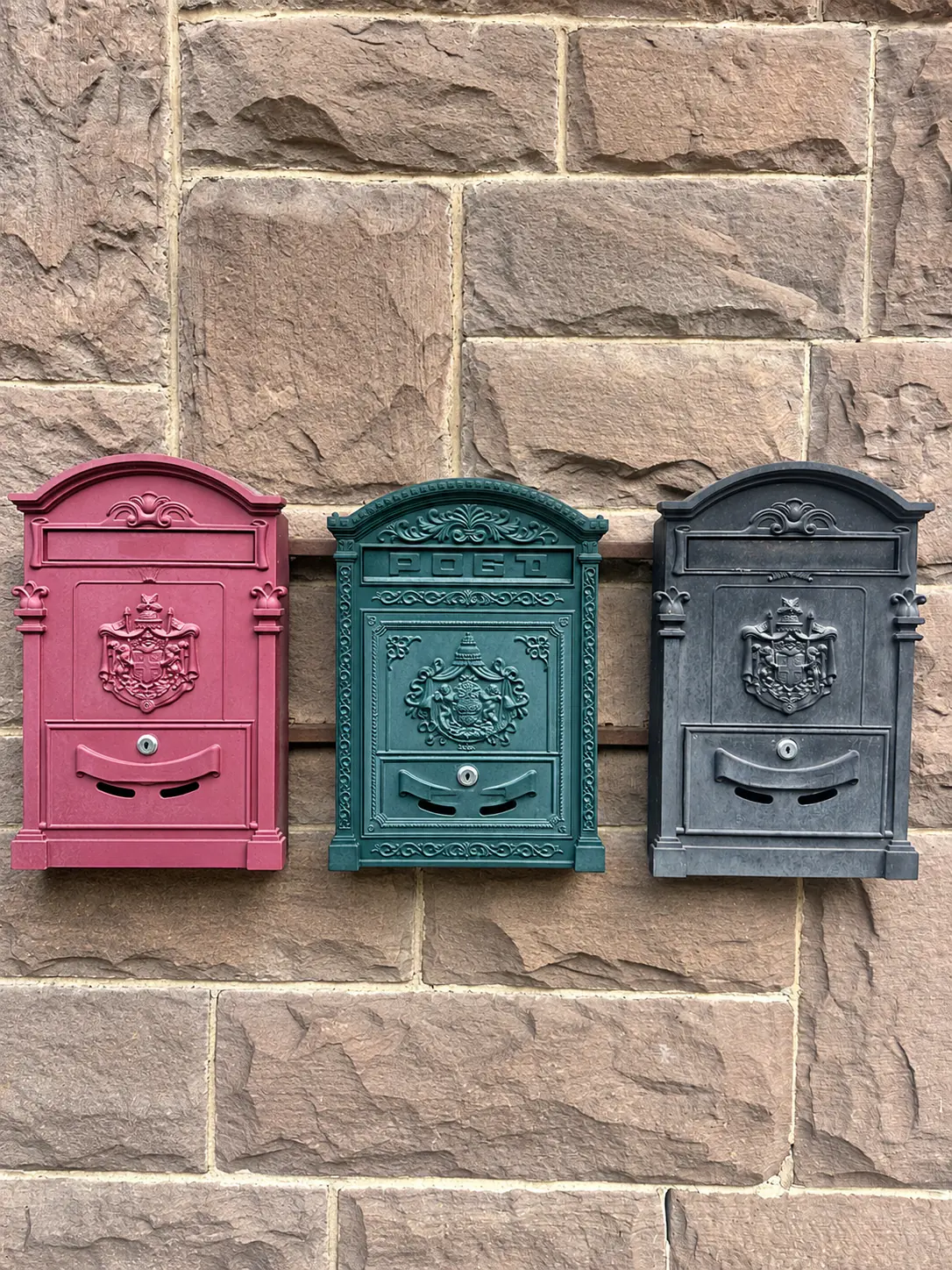 Three historic mailboxes in red, green and black on the sandstone wall of the old post office